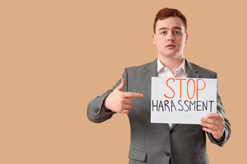 Young businessman pointing at paper with text STOP HARASSMENT on beige background