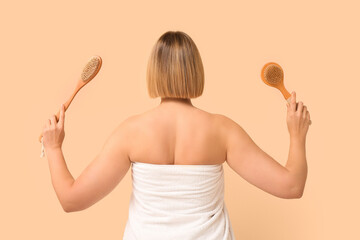 Beautiful young woman with body massage brushes on beige background, back view