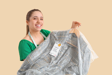 Female worker of dry-cleaner's with coat on beige background