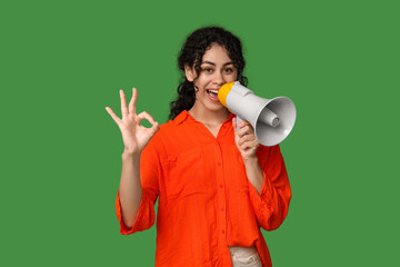 Young African-American woman with megaphone showing OK on green background