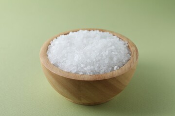 Organic white salt in bowl on olive background, closeup