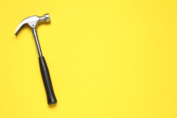 Hammer on yellow background, top view. Space for text