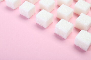 White sugar cubes on pink background, closeup. Space for text