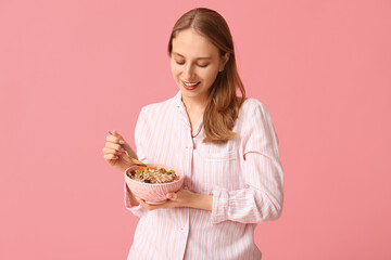 Young woman with bowl of healthy oatmeal on pink background