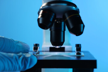 Scientist working with microscope on blue background, closeup