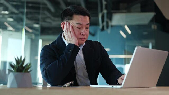 Man in formal outfit sitting in office and typing report on laptop while feeling tired. Frustrated male secretary reading results of work while resting head on hand and looking at computer screen.