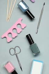 Nail polishes and set of pedicure tools on grey background, flat lay