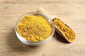 Curry powder in bowl and scoop on wooden table, closeup