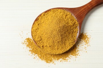 Curry powder in spoon on white wooden table, top view