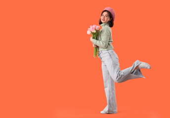 Portrait of fashionable young woman in beret with tulip flowers on orange background