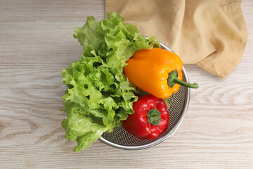 Colander with fresh lettuce and bell peppers on wooden table, top view