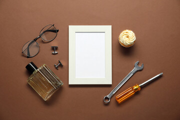 Empty photo frame, cupcake and men accessories on brown background, flat lay with space for text....