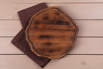 Cutting board and napkin on beige wooden table, top view