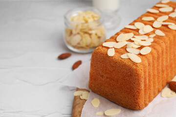 Cake with fresh almond flakes on white textured table, closeup. Space for text