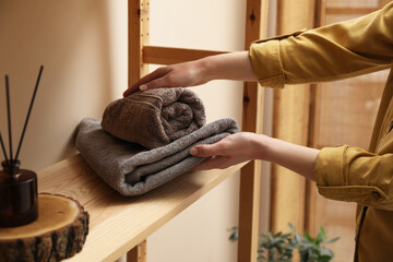 Woman putting towels onto shelf indoors, closeup