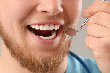 Male dentist with tool smiling on light background, closeup