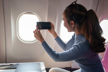 Asian female tourist checks notifications on smartphone while seated on airplane A businesswoman...
