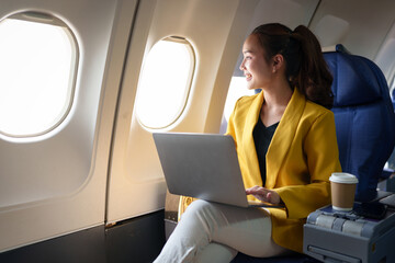 Confident businesswoman in formal clothes looking out of airplane window during flight while...