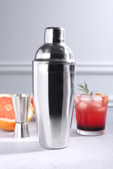 Metal shaker, delicious cocktail, jigger and grapefruit on light grey table