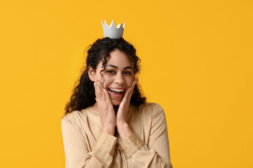 Beautiful young African-American woman in silver paper crown on yellow background