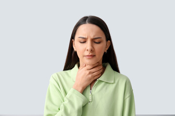 Beautiful young woman suffering from sore throat on grey background