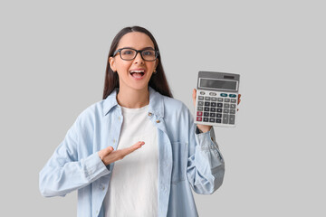 Happy young woman pointing at calculator on grey background