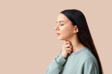 Beautiful young woman suffering from sore throat on brown background