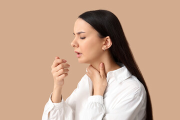 Beautiful young woman suffering from sore throat on brown background