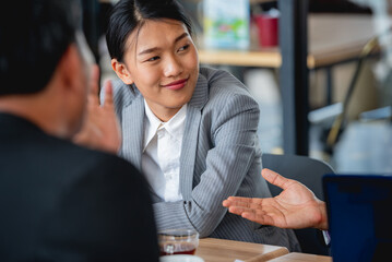 The image shows a young Asian businesswoman sitting at a table and talking to two colleagues.