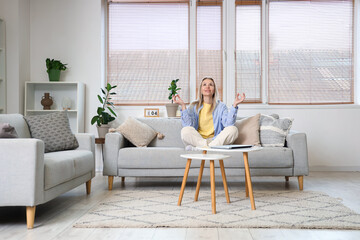 Young woman meditating on sofa in light living room