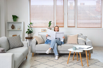 Young woman reading newspaper and sitting on sofa in light living room