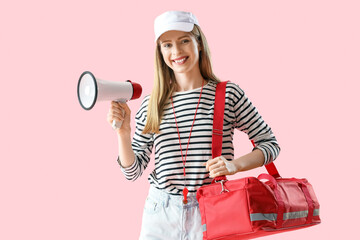 Young female lifeguard in cap with megaphone and first aid kit on pink background