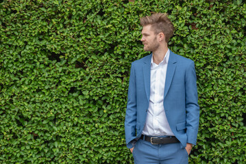A man in a blue suit is standing in front of a green wall.