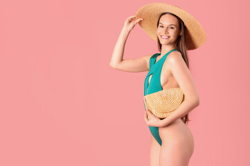 Smiling woman in swimming suit and hat with bag on pink background