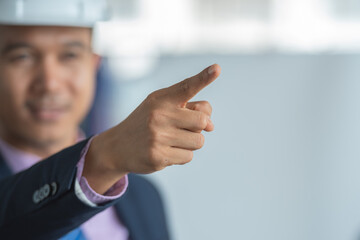 A businessman in a hard hat is pointing at something.