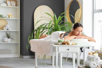 Beautiful Asian woman with mud on her shoulders lying in spa salon