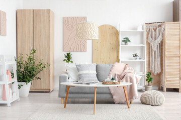 Light interior of stylish living room with sofa, houseplants, shelving unit and coffee table