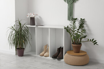 Interior of stylish hall with shelving unit, shoes and bouquet of flowers near white wall