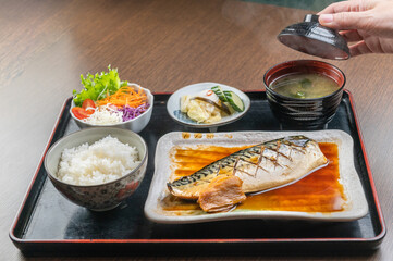 A delicious Japanese meal of grilled mackerel with rice, miso soup, and pickled vegetables.