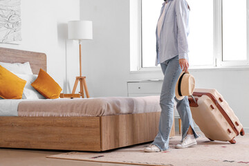 Woman with suitcase and hat in hotel room