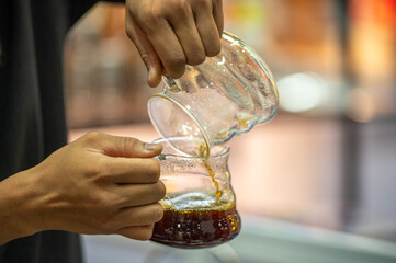 The barista carefully pours the coffee from one glass container to another.