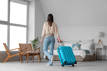 Woman with suitcase, passport and tickets in light hotel room, back view