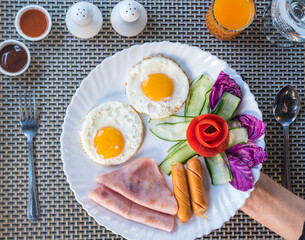 A plate with two eggs, ham, sausage, cucumber, and tomato.