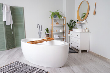 Stylish interior of modern bathroom with bathtub, rug and chest of drawers