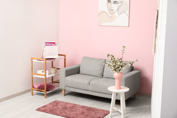 Vase with beautiful blooming branches on table and sofa at home