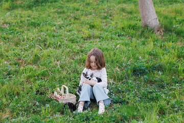 A young girl sits in a grassy field holding a rabbit in her arms. The scene is peaceful and serene,...