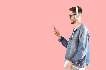 Young bearded man in headphones with mobile phone listening to music on pink background