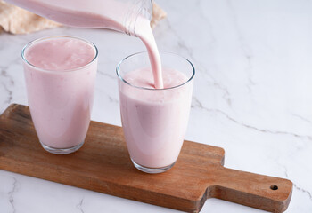 Pouring homemade fruit kefir, buttermilk or yogurt with probiotics. Yogurt flowing from glass bottle on light background. Probiotic cold fermented dairy drink. Trendy food and drink. Copy space