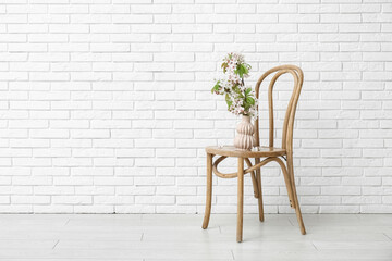 Vase with blossoming branches on chair near white brick wall in room