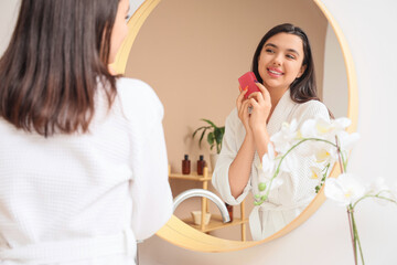 Young woman with soap near mirror in bathroom